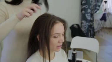 Genç bir kadın bir Kuaför koltukta oturur: Kuaför saç şekillendirme yapar. Genç sarışın kadın şık bir saç modeli yapmak için güzellik salonuna geldi.