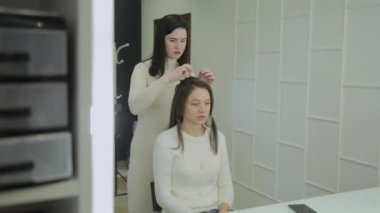 Genç bir kadın bir Kuaför koltukta oturur: Kuaför saç şekillendirme yapar. Genç sarışın kadın şık bir saç modeli yapmak için güzellik salonuna geldi.