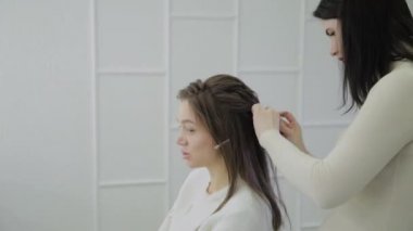 Genç bir kadın bir Kuaför koltukta oturur: Kuaför saç şekillendirme yapar. Genç sarışın kadın şık bir saç modeli yapmak için güzellik salonuna geldi.