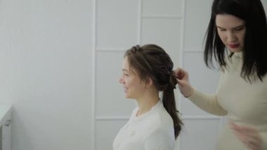 Genç bir kadın bir Kuaför koltukta oturur: Kuaför saç şekillendirme yapar. Genç sarışın kadın şık bir saç modeli yapmak için güzellik salonuna geldi.