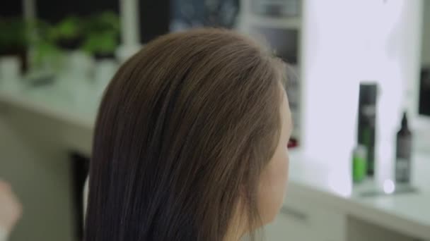 Une jeune femme s'assoit dans un fauteuil de coiffeur : un coiffeur fait une coiffure. Une jeune femme blonde est venue au salon de beauté pour faire une coiffure élégante . — Video