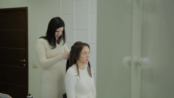 Eine junge Frau sitzt im Friseursessel, ein Friseur frisiert. eine junge blonde Frau kam in den Schönheitssalon, um sich eine stylische Frisur zu machen. — Stockvideo