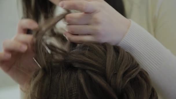 Een jonge vrouw zit in een fauteuil kappers: een kapper doet een haar styling. Een jonge blonde vrouw kwam naar de salon van de schoonheid te maken van een stijlvol kapsel. — Stockvideo