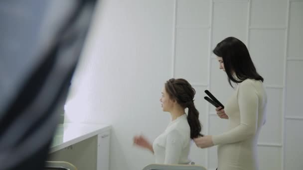 茶色の髪の美しい女性はカーリング アイロン美容師によって治療しています。ハンドヘルドのリアルタイム エスタブリッシング ・ ショット. — ストック動画