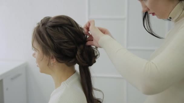 Uma jovem se senta em uma poltrona de cabeleireiro: um cabeleireiro faz um estilo de cabelo. Uma jovem mulher de cabelos justos veio ao salão de beleza para fazer um penteado elegante . — Vídeo de Stock