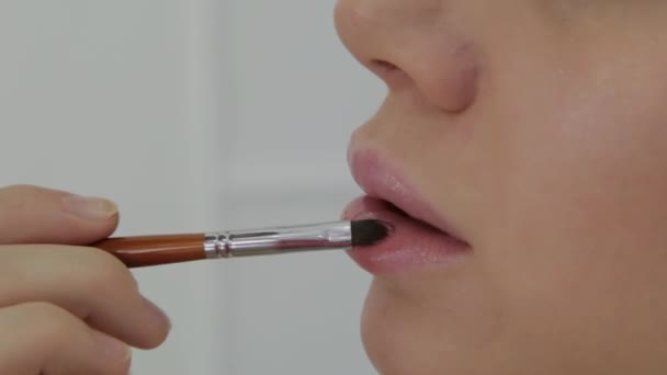 Truccatore utilizzando pennello per l'applicazione rossetto sulle labbra bella donna. Luminosità di labbro di applicazione vicina su modello di moda di labbra. Visagiste che si trucca le labbra. Concetto bellezza . — Video Stock