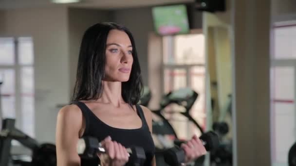 Beautiful athletic young girl trains dumbbells biceps in the gym. — Stock Video