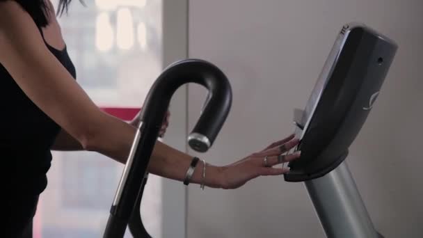 Belle jeune fille sportive fait des réglages sur un entraîneur elliptique dans la salle de gym . — Video
