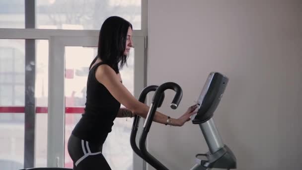 Beautiful athletic young girl makes settings on an elliptical trainer in the gym. — Stock Footage Beautiful athletic young girl makes settings on an elliptical trainer in the gym. Stock Video