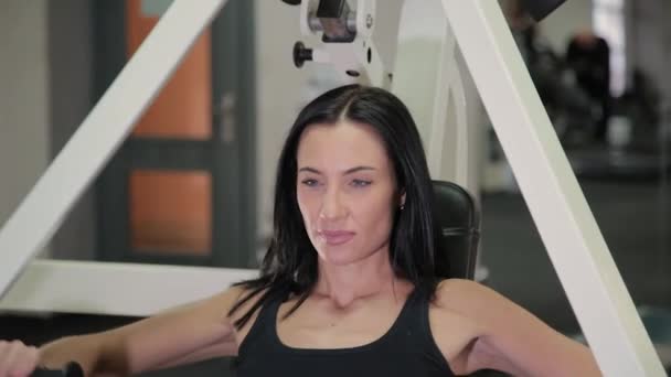 Hermosa mujer morena deportiva se dedica a un simulador para los músculos del pecho y los brazos. Concepto de estilo de vida . — Vídeos de Stock