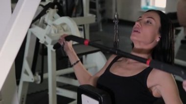 Güzel atletik genç kız göğüs simülatör spor salonunda bir çekme gerçekleştirir.
