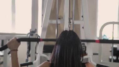 Güzel atletik genç kız göğüs simülatör spor salonunda bir çekme gerçekleştirir.