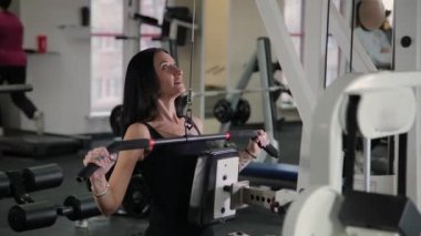 Güzel atletik genç kız göğüs simülatör spor salonunda bir çekme gerçekleştirir.