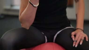 Oturan genç sportif kadın top ve kaldırma dumbbells eğitim pazı sırasında spor salonunda uygun..