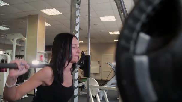 Όμορφη αθλητική νεαρή κοπέλα crouches στους ώμους στο γυμναστήριο. — Αρχείο Βίντεο