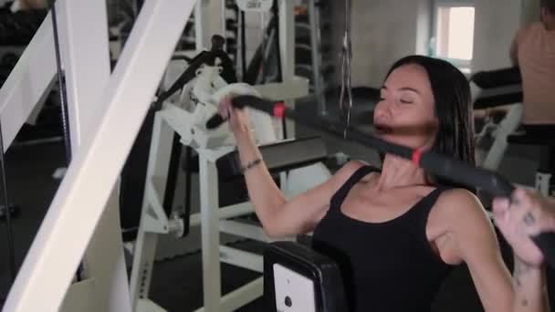 Mooi sportieve jonge meisje voert een pull op de simulator van de borst in de sportschool. — Stockvideo