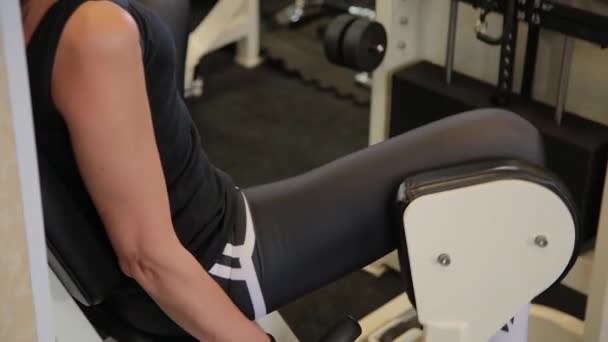 У спортзалі жінка розсовує ноги на симуляторі. Спортсменка сидить на тренувальному сидінні і притискає зовнішню поверхню стегон до подушок . — стокове відео