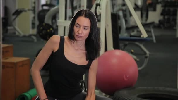 Joven mujer deportiva sentada en la pelota en forma y levantando pesas mientras entrena bíceps en el gimnasio . — Vídeos de Stock