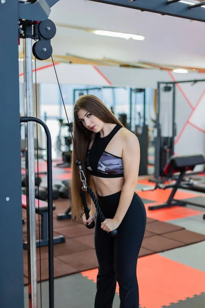 Κορίτσι σε ένα γυμναστήριο κάνει ασκήσεις τρικέφαλος μύς στο μπλοκ exerciser. — Φωτογραφία Αρχείου