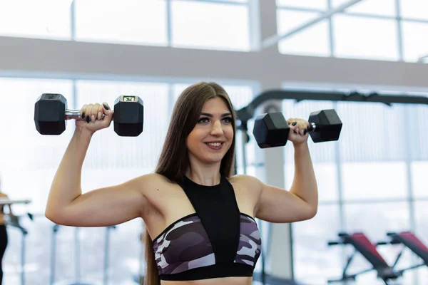 Très belle fille trains épaules avec haltères sur le banc dans la salle de gym . — Photo