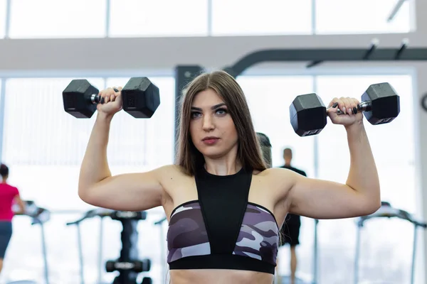 Très belle fille trains épaules avec haltères sur le banc dans la salle de gym . — Photo