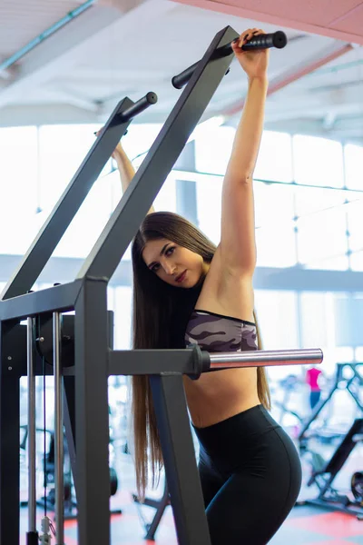 Mujer joven entrenando en el gimnasio. Tirando de la gravitrona . — Foto de Stock
