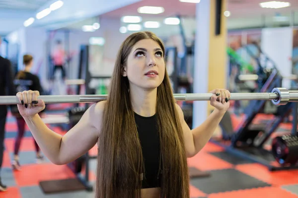 Beautiful girl crouches with a barbell on the shoulders in the gym.