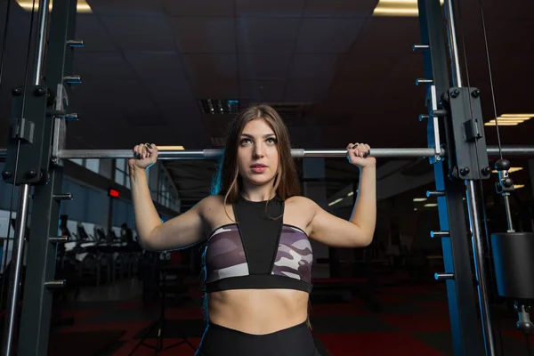 Beau modèle de fitness sexy secoue un haltère assis derrière la tête dans la salle de gym . — Photo