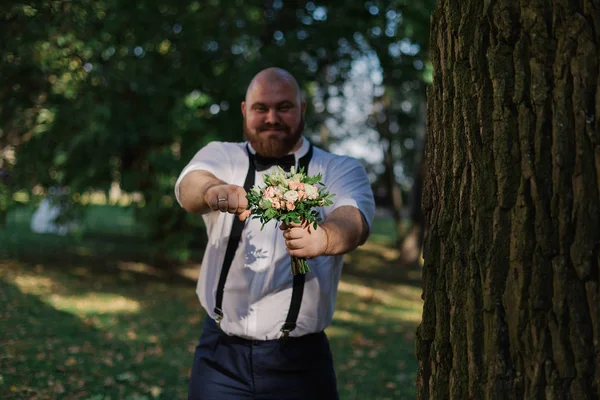 Elegante noivo gordo barbudo com buquê de casamento no parque . — Fotografia de Stock