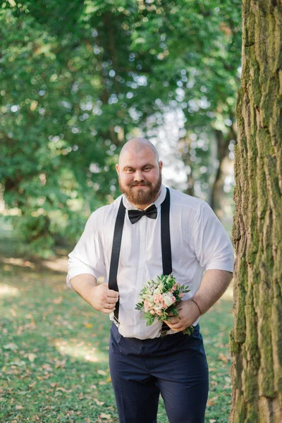 时尚的胡须脂肪新郎与婚礼花束在公园. — 图库照片