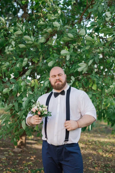 Elegante barbuto grasso sposo con bouquet da sposa nel parco . — Foto Stock