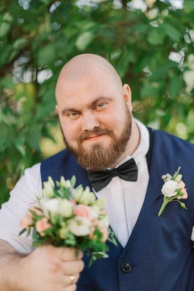 Elegante novio gordo barbudo con ramo de bodas en el parque . — Foto de Stock