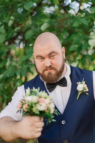 Elegante novio gordo barbudo con ramo de bodas en el parque . —  Fotos de Stock