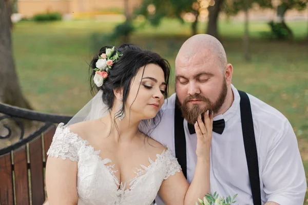 Recién casados se sientan en un banco en el parque . — Foto de Stock