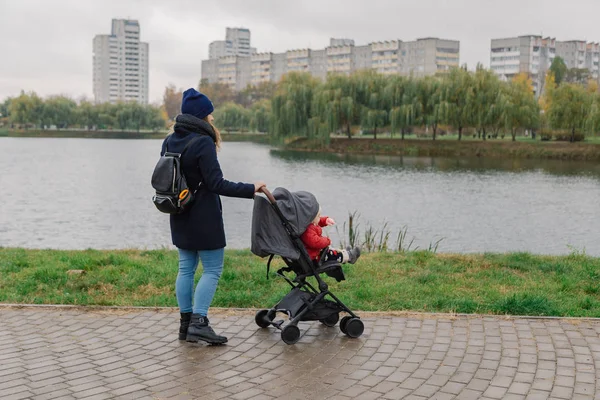 Женщина гуляет в парке с коляской и маленьким ребенком у озера . — стоковое фото