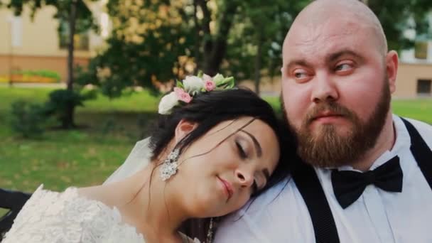 Tinerii căsătoriți fericiți stau pe o bancă în parc . — Videoclip de stoc