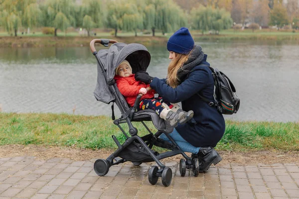 Kobieta przechadza się w parku z wózka i małe dziecko w pobliżu jeziora. — Zdjęcie stockowe