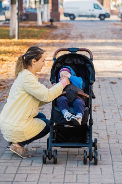 Bir kadın bir çocuk arabasındaki bebek ile parkta güneşli bir günde yürür..