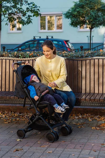 Женщина с ребенком в коляске сидит на скамейке в солнечный день . — стоковое фото
