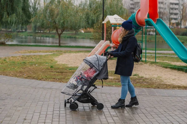 Una mujer camina por el parque con un cochecito y un niño . — Foto de Stock