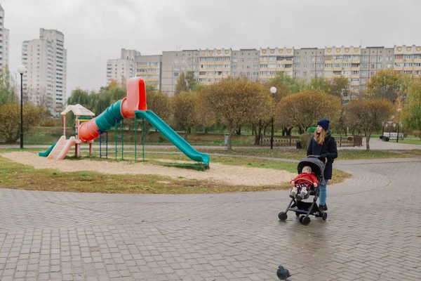 Uma mulher caminha no parque com um carrinho e uma criança pequena . — Fotografia de Stock