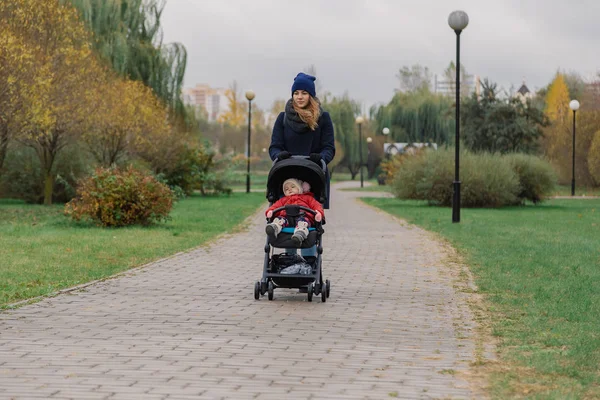 Egy nő sétál a parkban a babakocsi, és egy kis gyerek. — Stock Fotó