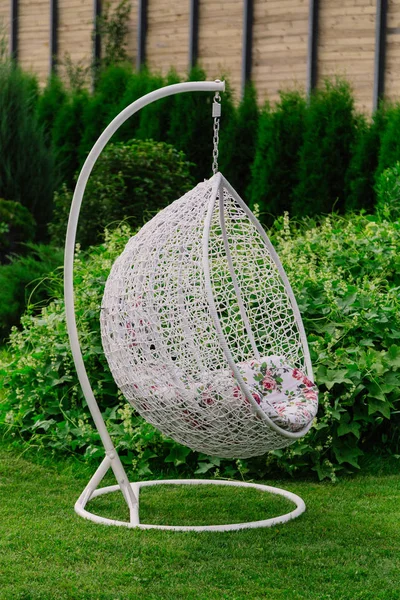 Suspended white cocoon chair on green grass.