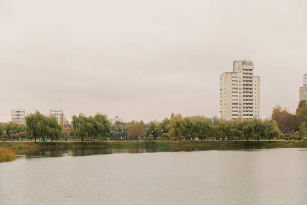 Costa gramada do lago com edifícios residenciais à distância, em um dia nublado, clima de outono . — Fotografia de Stock