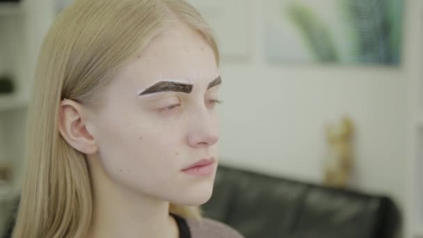 Belle jeune fille dans un salon de beauté attend que la peinture des sourcils soit absorbée . — Video