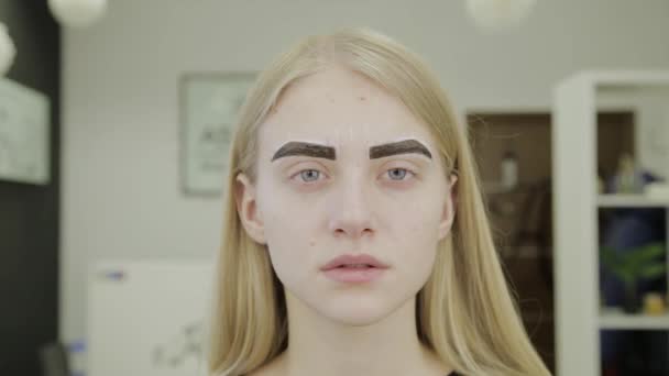 Belle jeune fille dans un salon de beauté attend que la peinture des sourcils soit absorbée . — Video