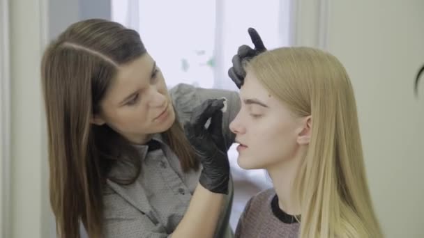 Limpe as sobrancelhas com um disco de algodão para uma jovem após o procedimento de coloração . — Vídeo de Stock