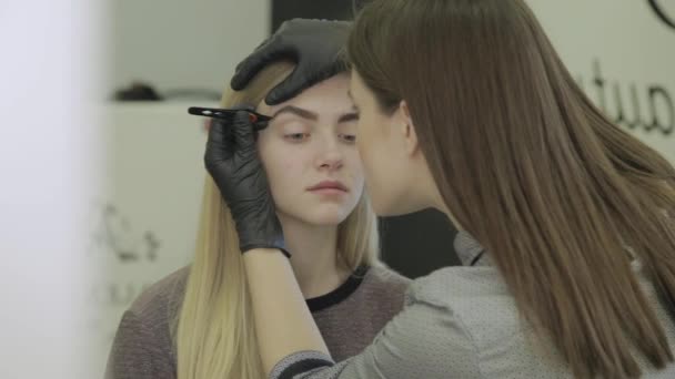 Make-up artiest plucks de wenkbrauwen van een jong meisje in een schoonheidssalon. — Stockvideo