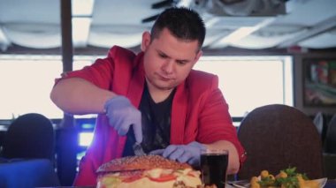 Bir adam büyük bir burger bir bıçakla keser..