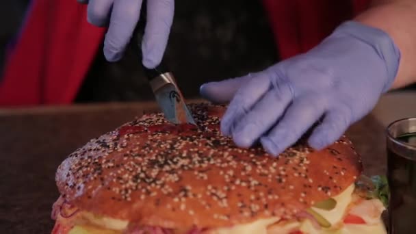 Um homem corta um hambúrguer enorme com uma faca . — Vídeo de Stock